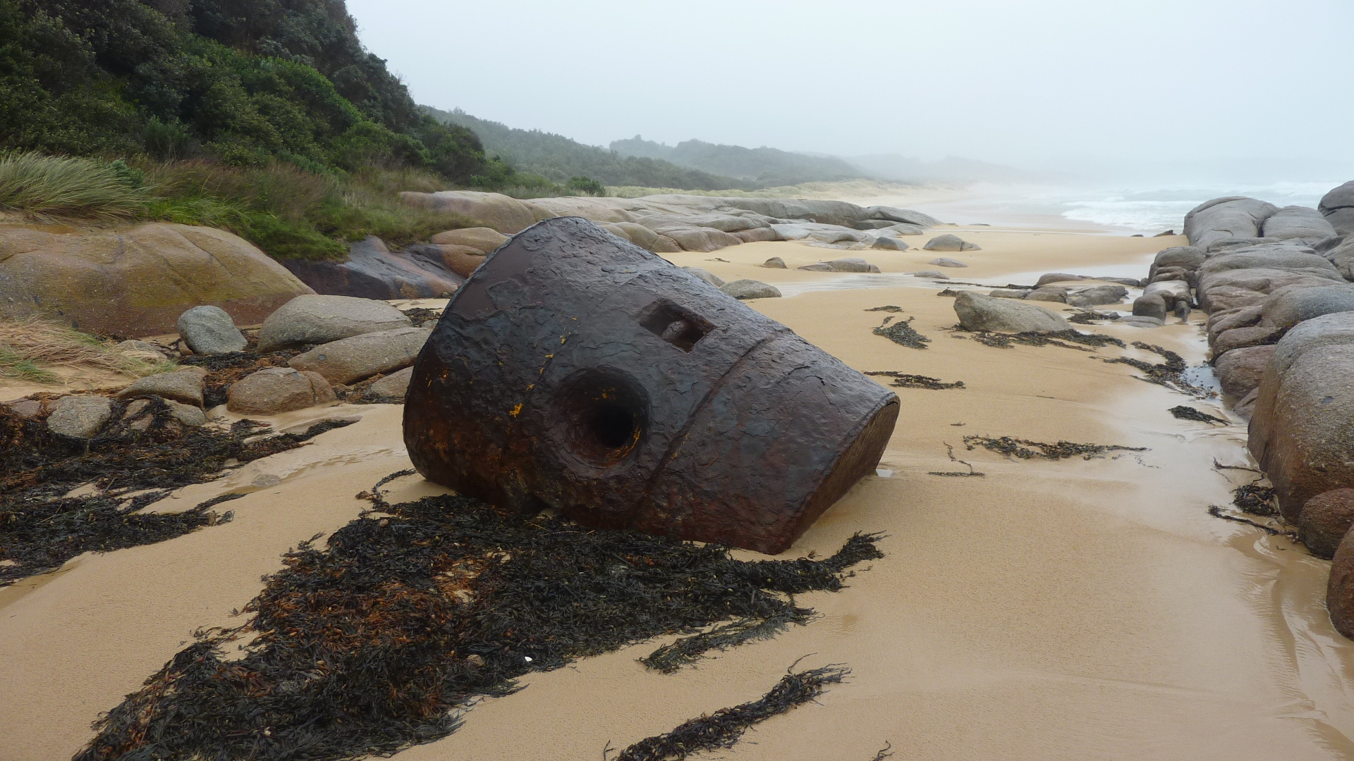 Image shows a cylindrical piece of wreckage on a beach  