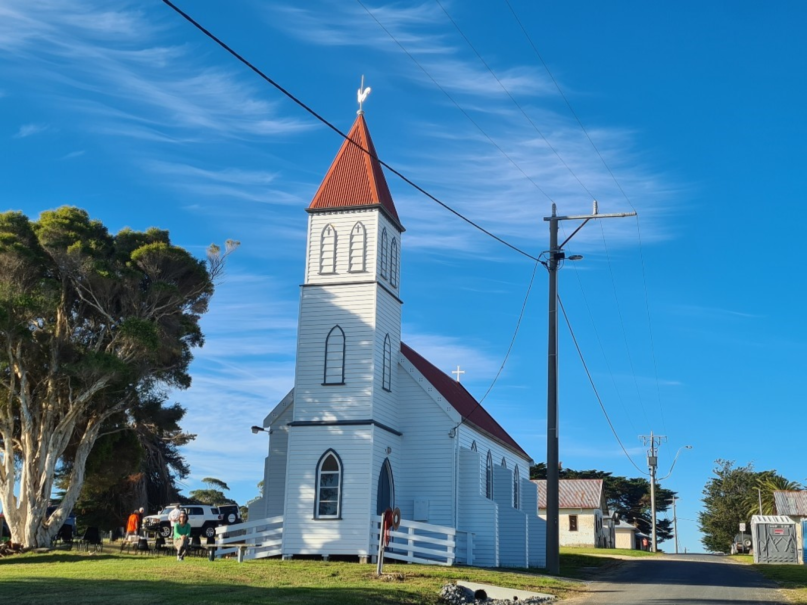 The church can be seen from a distance. The church is white with a red roof. The sun shine over the roof. 