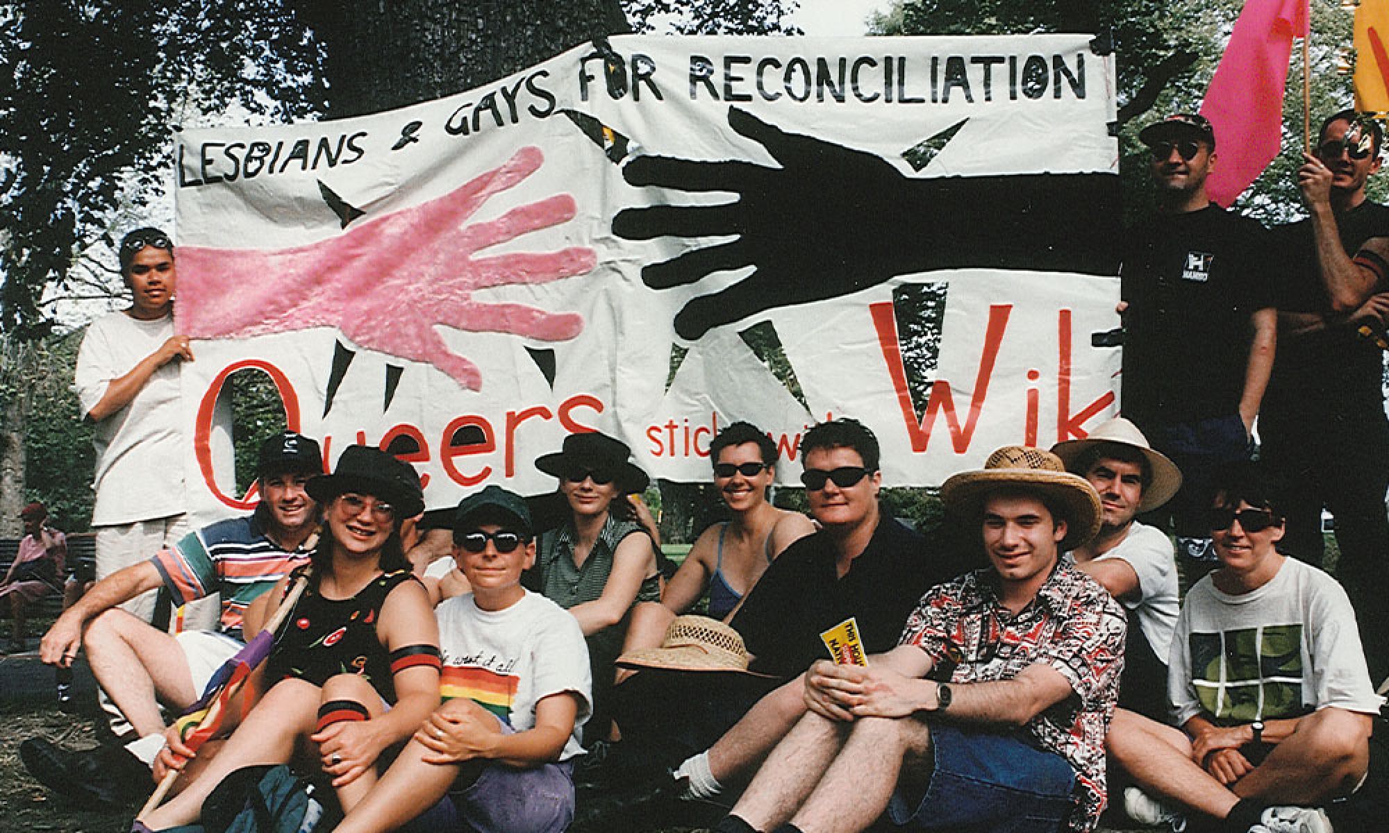 The image shows a group of people from the LGBTQI+ community holding up a flag that reads ' Lesbians and Gays for Reconciliation'.
