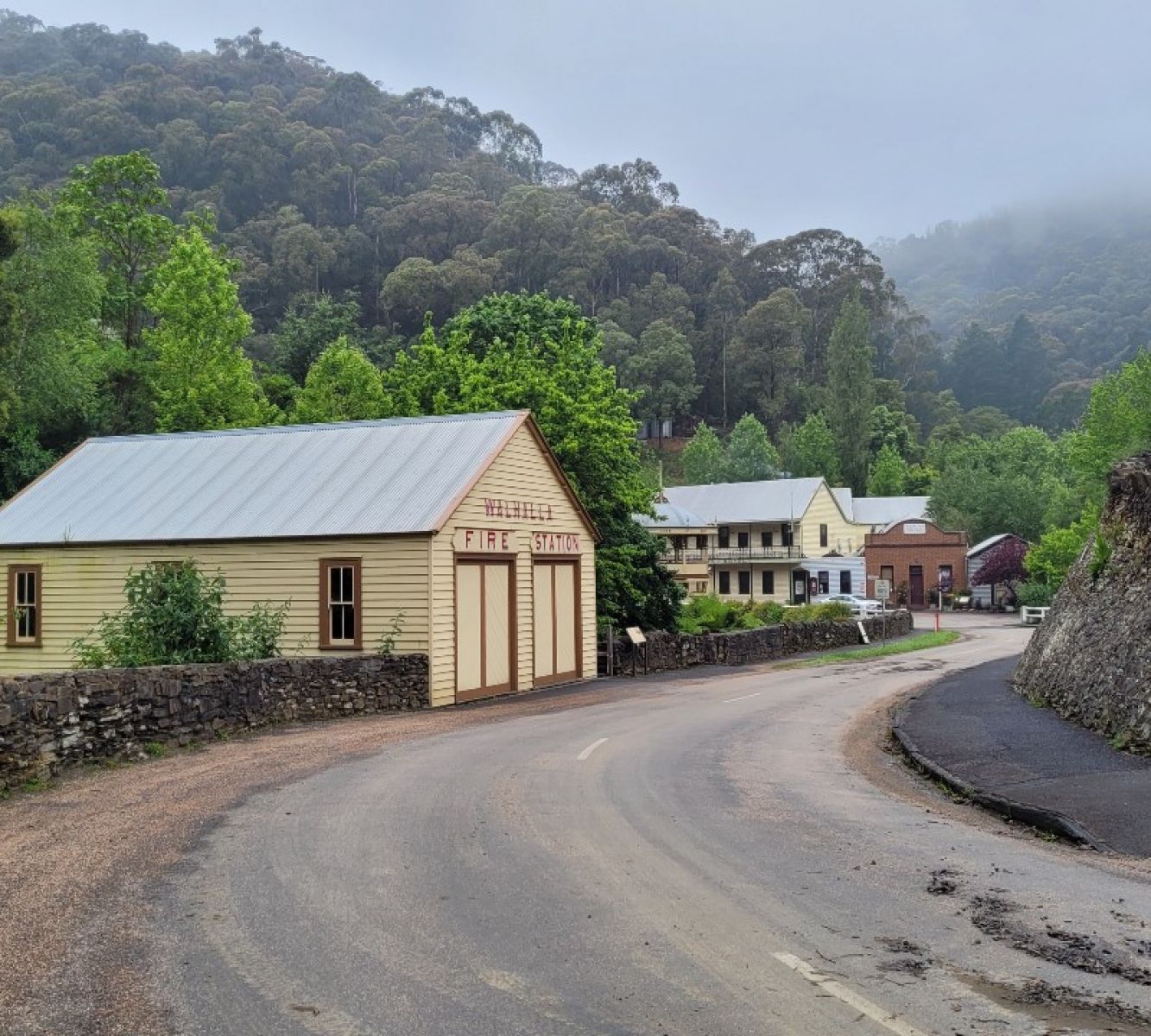 Image shows the road into Walhalla. A roadhouse is beside the road with mountains and trees. A fog covers the mountain tops. 