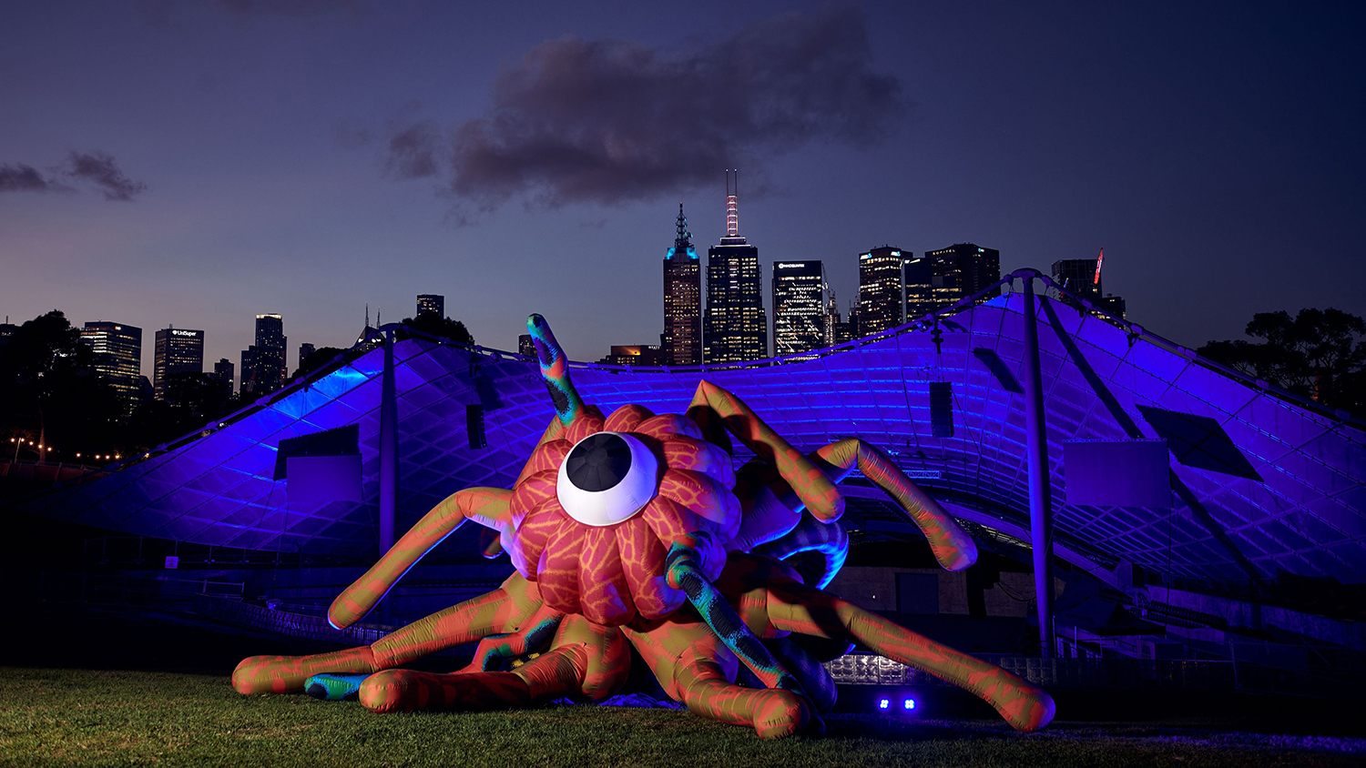 Image shows illuminated octopus in front of Melbourne city buildings at night time  