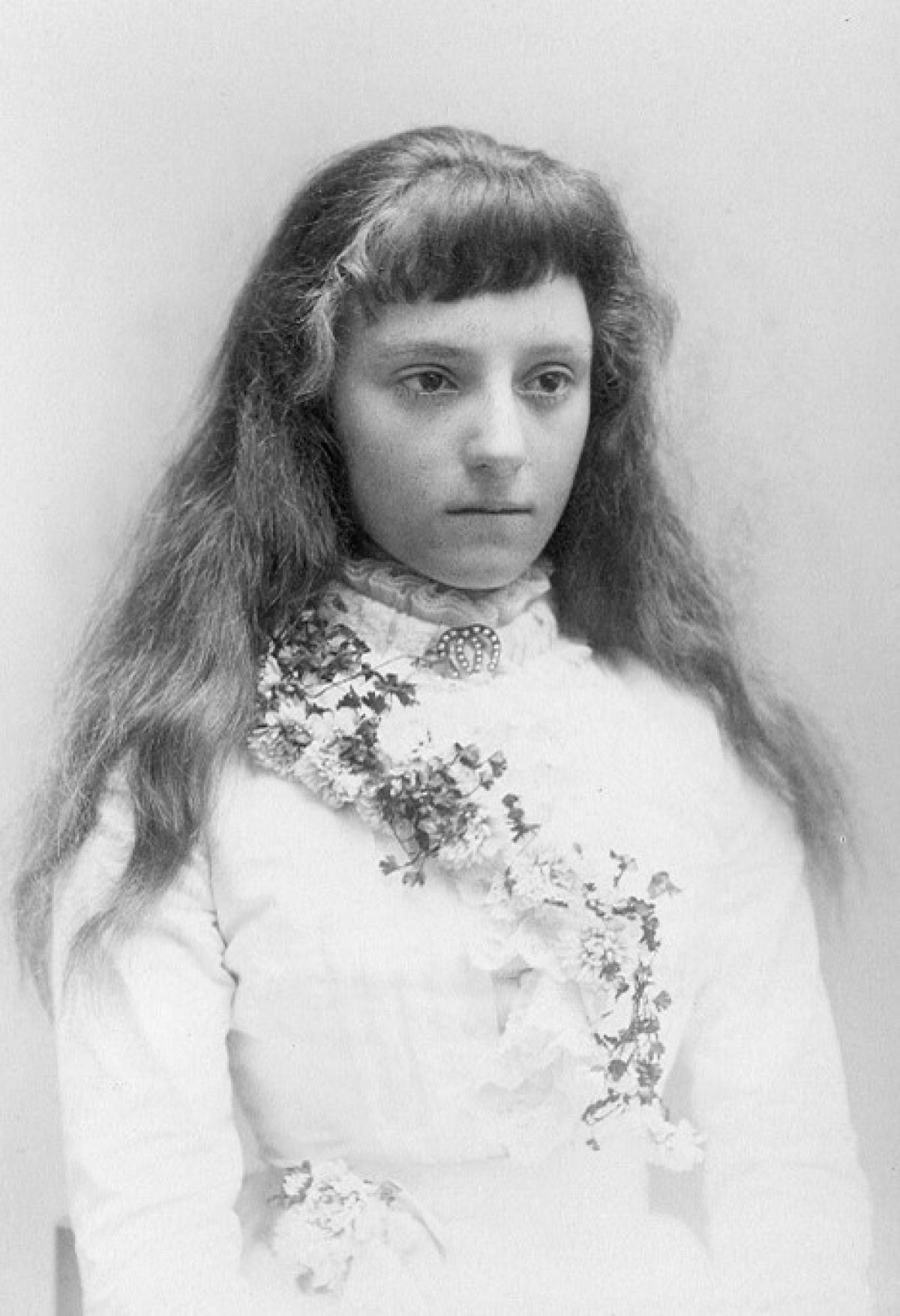 The portrait shows Laura not looking at the camera, her hair is down and over her shoulders. She wears a white dress and flower decoration draped over her left shoulder.