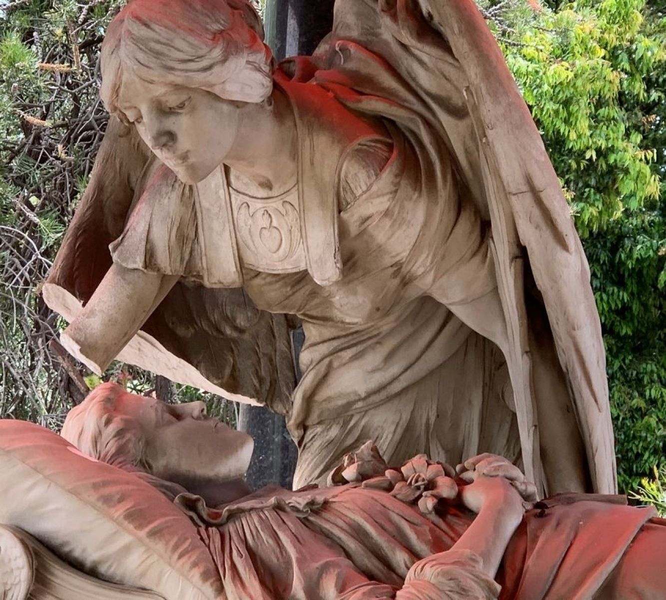 Two memorial statues can be seen in the image. An angel looks over a sick person as they lay in bed. 